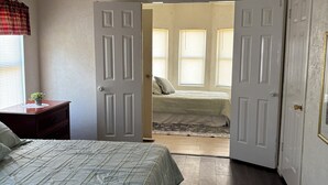 A bedroom with a bed, a nightstand, a ceiling fan, and a door leading to another room. - Quiet Kentucky Retreat • Clean, Comfortable (Williamsburg)