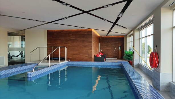 Ein Hallenbad mit gefliestem Rand, einer Holzwand und einer Glaseinfassung auf einer Seite.