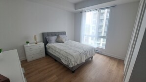 Ein Schlafzimmer mit Bett, Nachttisch, Kommode und einem Fenster mit Vorhängen.