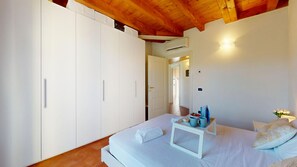 Une chambre à coucher avec un lit, une table de chevet sur laquelle se trouve un plateau, une armoire blanche et un plafond en bois.