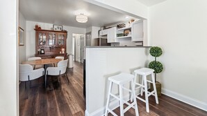 Une cuisine moderne avec des meubles blancs, une table à manger en bois et deux tabourets de bar blancs.