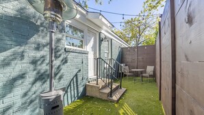 Un espace patio agrémenté d’un mur en briques, d’un escalier en béton menant à une porte blanche et d’une petite table avec des chaises.