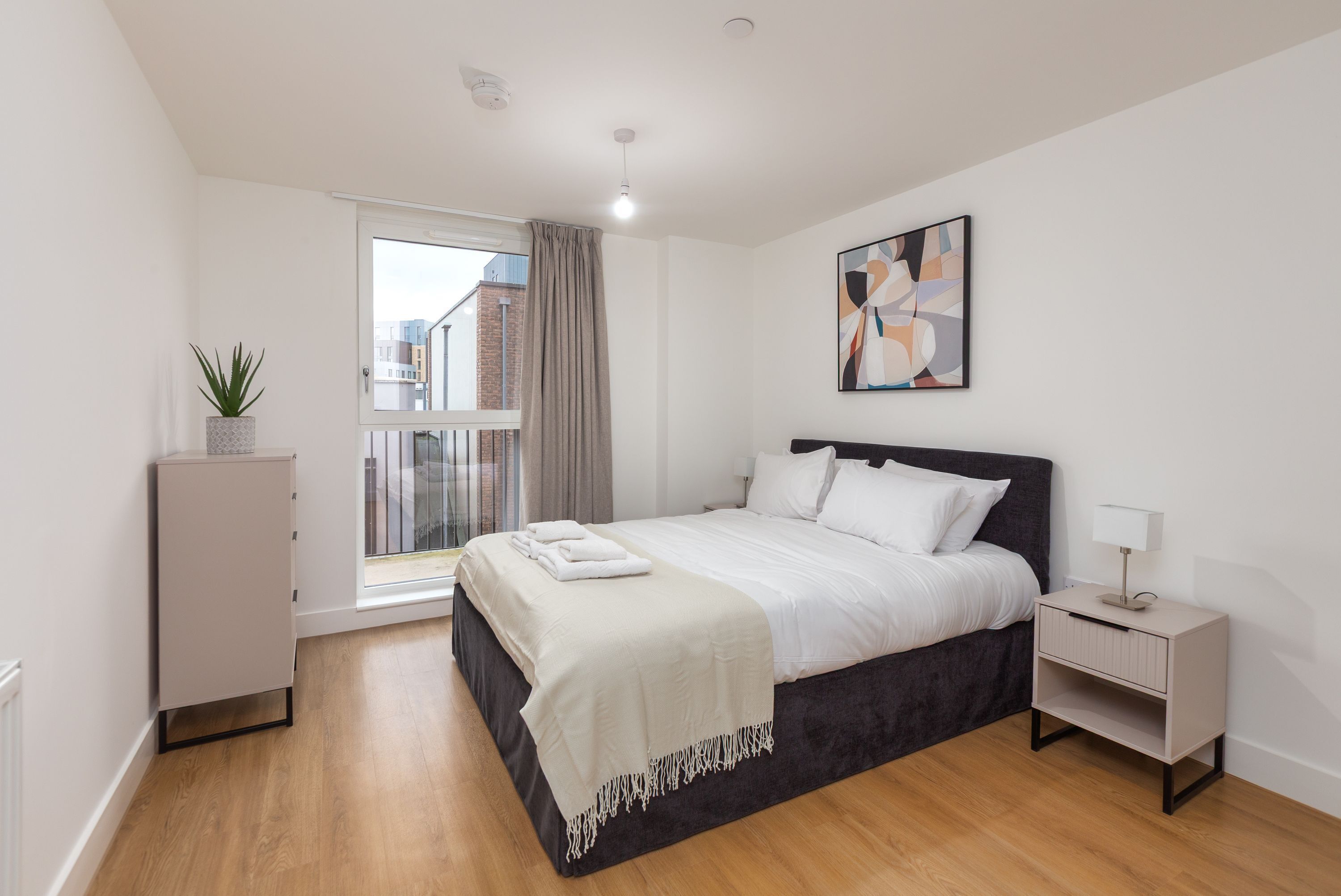 A bedroom with a bed, bedside table, lamp, and a window with curtains.