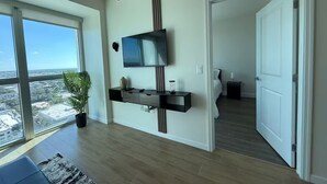 A modern living room with a large window, a mounted TV, and a plant. - Downtown Skyline Suite- Breathtaking view (Fort Myers)