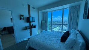 A hotel room with a large bed, a TV mounted on the wall, and a view of the city through large windows. - Downtown Skyline Suite- Breathtaking view (Fort Myers)