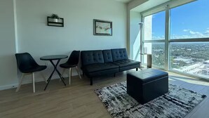 A modern living room with a black sofa, two black chairs, a small round table, and a large window offering a city view. - Downtown Skyline Suite- Breathtaking view (Fort Myers)