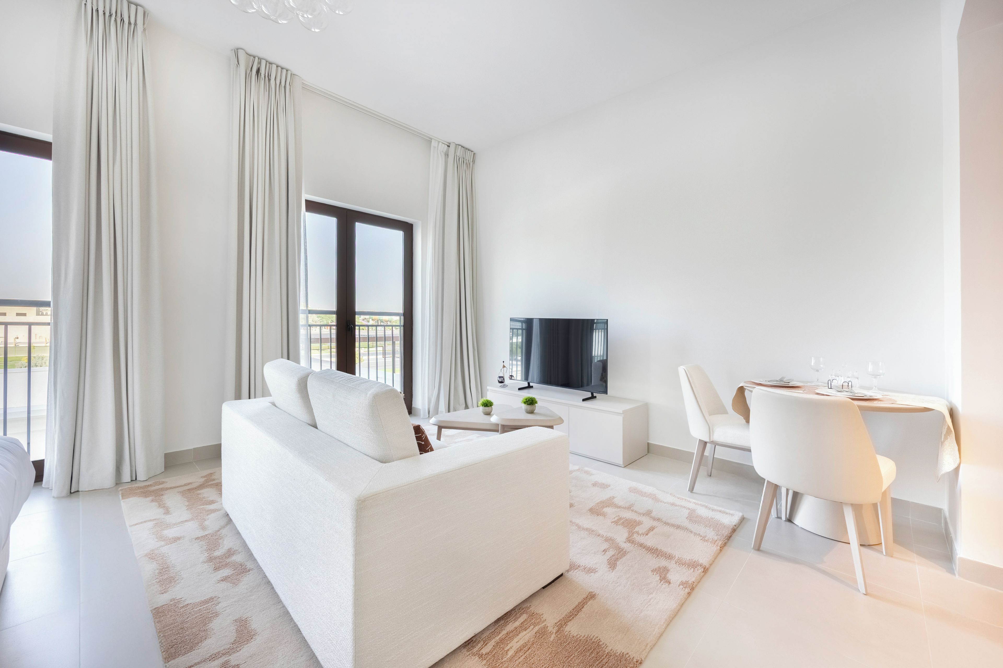 A modern living room with a sofa, a TV, a dining table with chairs, and a balcony view.