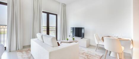 A modern living room with a sofa, a TV, a dining table with chairs, and a balcony view.