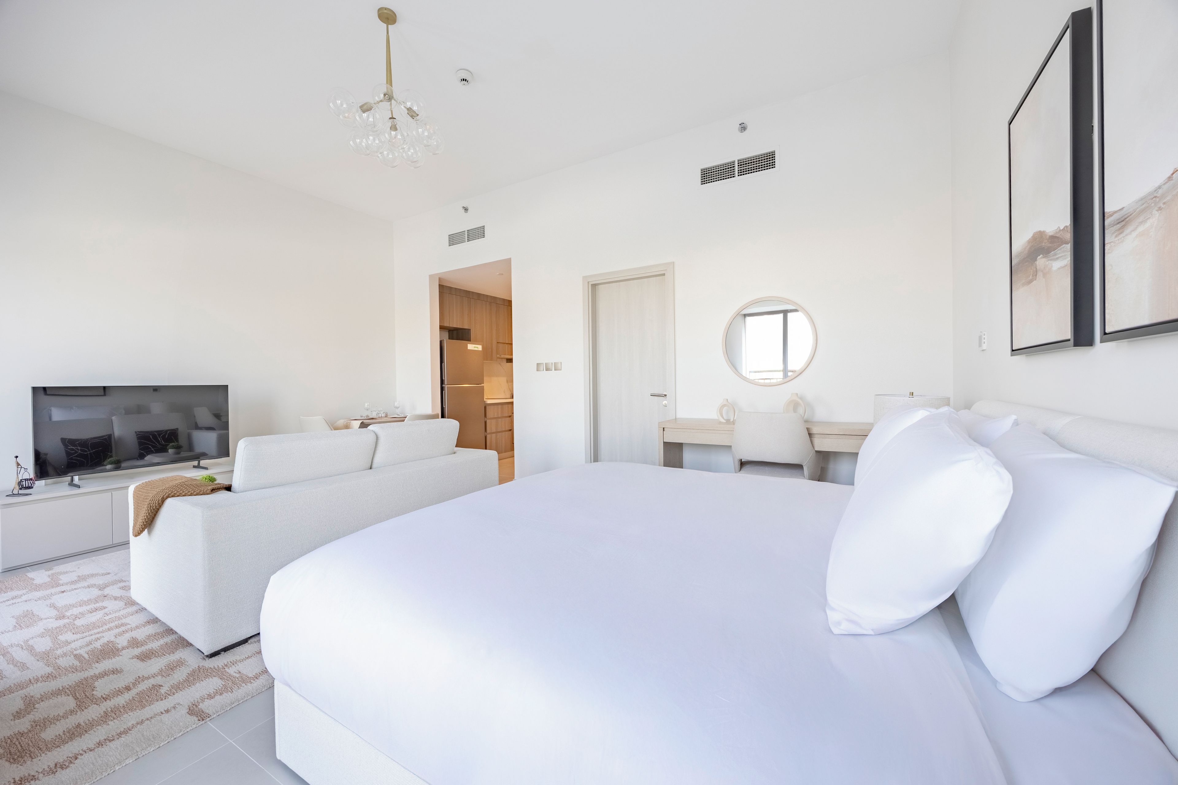 A modern hotel room with a large bed, a television, a desk, and a dining area.
