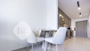 A modern kitchen with built-in appliances and a dining area with white chairs and a table. - 224-Bloomfields Modern Stu Yas Golf  (Abu Dhabi)