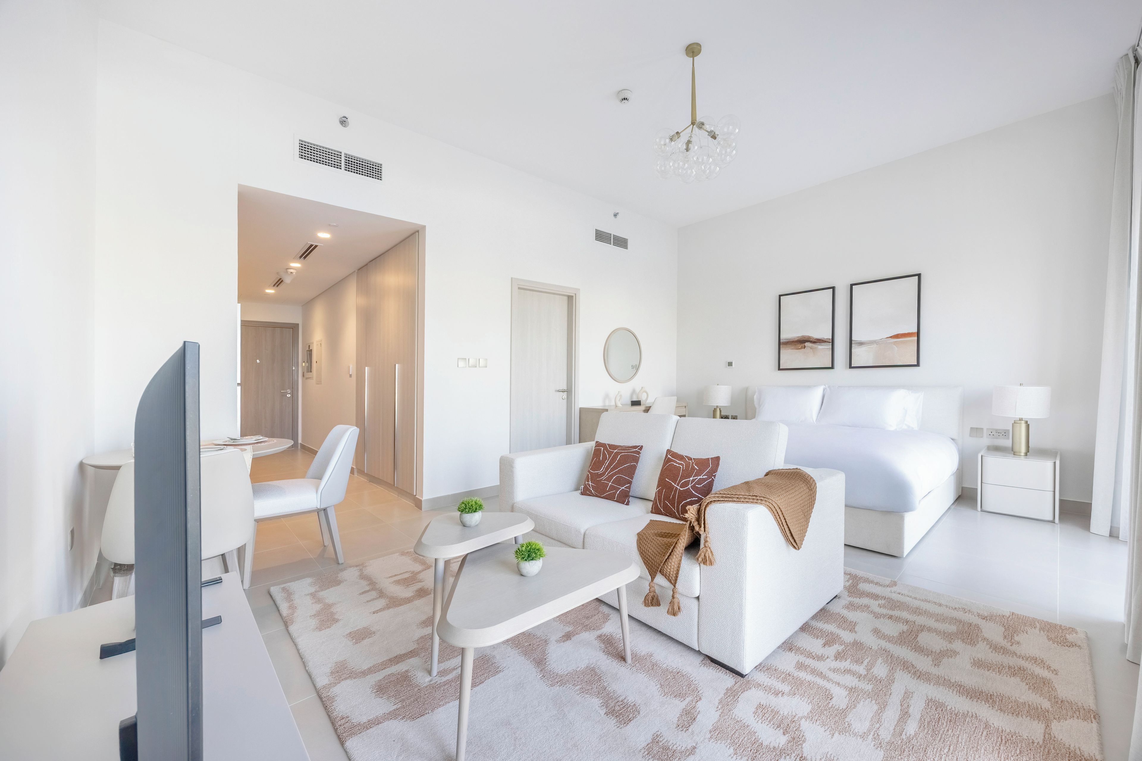 A modern, well-lit living room with a sofa, coffee table, and a TV. There is a hallway leading to another room.