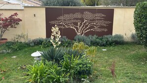 A garden with a variety of plants, a decorative wall with a tree design, and a stone sculpture. - Charming villa for a vacation in the south of France (Uzès)