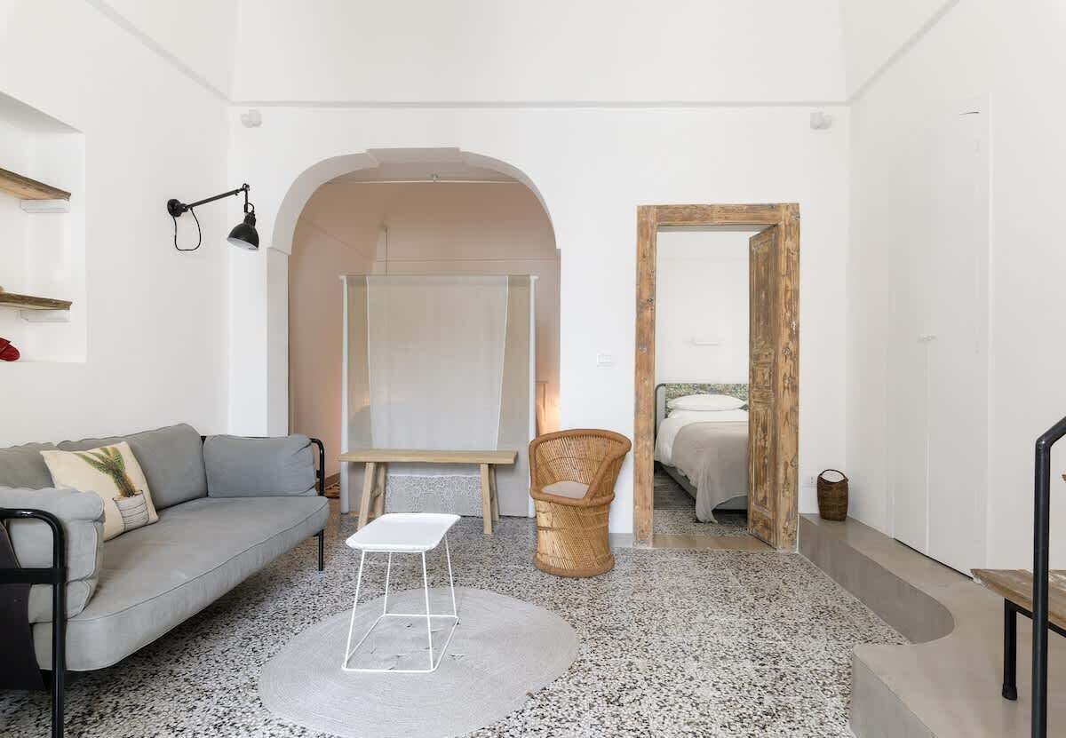 Una sala de estar moderna con un sofá gris, una mesa de centro blanca, una silla de mimbre y un espejo grande.