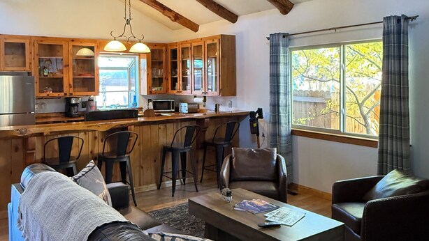 A cozy living room with a sofa, coffee table, and a view of the kitchen. - Woodsy Cozy Escape, Finest Mountain Vibes, Hot Tub, Pirate Ship and Xbox (Big Bear City)