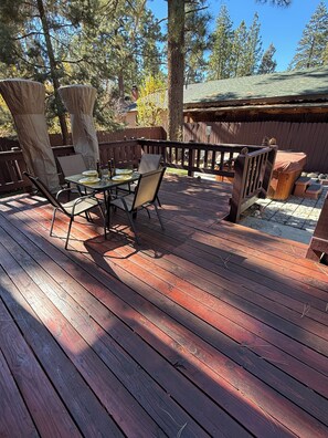 Een houten terras met een tafel en stoelen, omgeven door een houten hek en bomen.