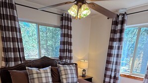 A bedroom with a large bed, a ceiling fan, and curtains. - Woodsy Cozy Escape, Finest Mountain Vibes, Hot Tub, Pirate Ship and Xbox (Big Bear City)
