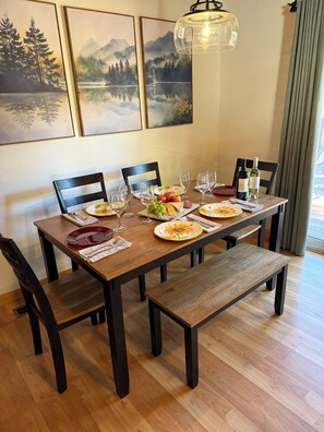 Een eettafel gedekt met borden, glazen en een fles wijn, omringd door stoelen.