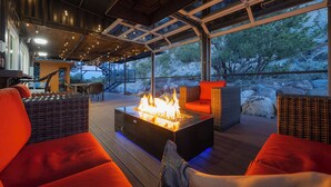Una amplia terraza al aire libre con una chimenea, mobiliario de mimbre y vistas del paisaje circundante.