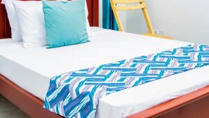 A neatly made bed with a patterned blanket, a wooden headboard, and a wooden chair beside it. - 1 - Single room at Mufasha Boutique And Suites (Kisoro)