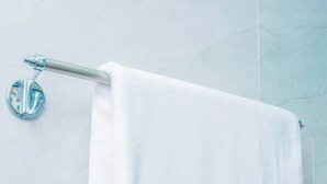 A white towel hanging on a metal towel rack in a bathroom with light blue tiles. - 1 - Single room at Mufasha Boutique And Suites (Kisoro)