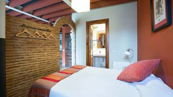 A bedroom with a bed, a brick wall, wooden beams, a hanging light fixture, and a framed picture on the wall.