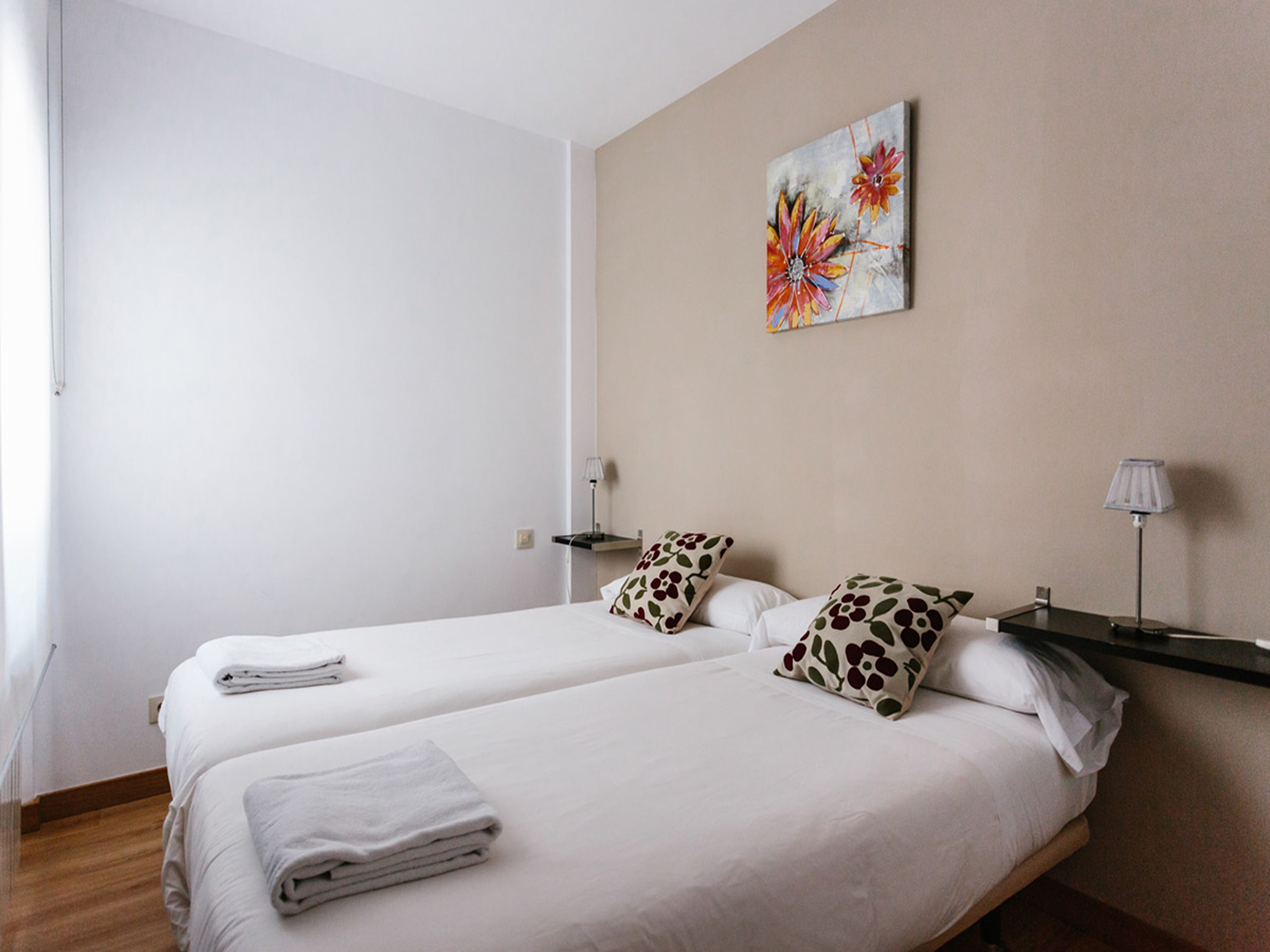 Ein Hotelzimmer mit zwei Betten, weißen Leintüchern, einem Bild an der Wand und Nachttischlampen.