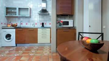 A compact kitchen with a washing machine, microwave, and wooden cabinets.