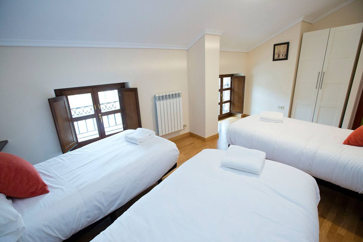 A hotel room with two single beds, a wooden floor, a radiator, and a window with a view.