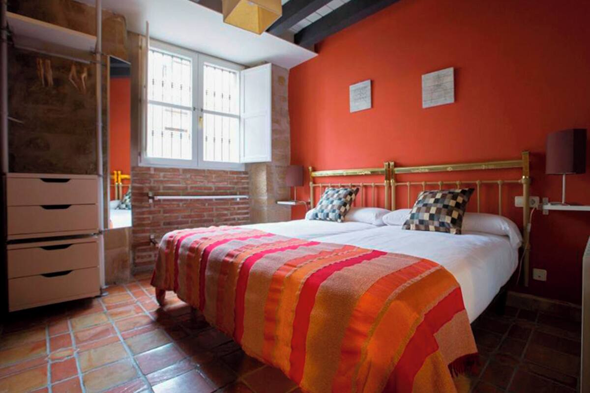 A bedroom with a brick wall, a bed with a striped blanket, and a window with white shutters.
