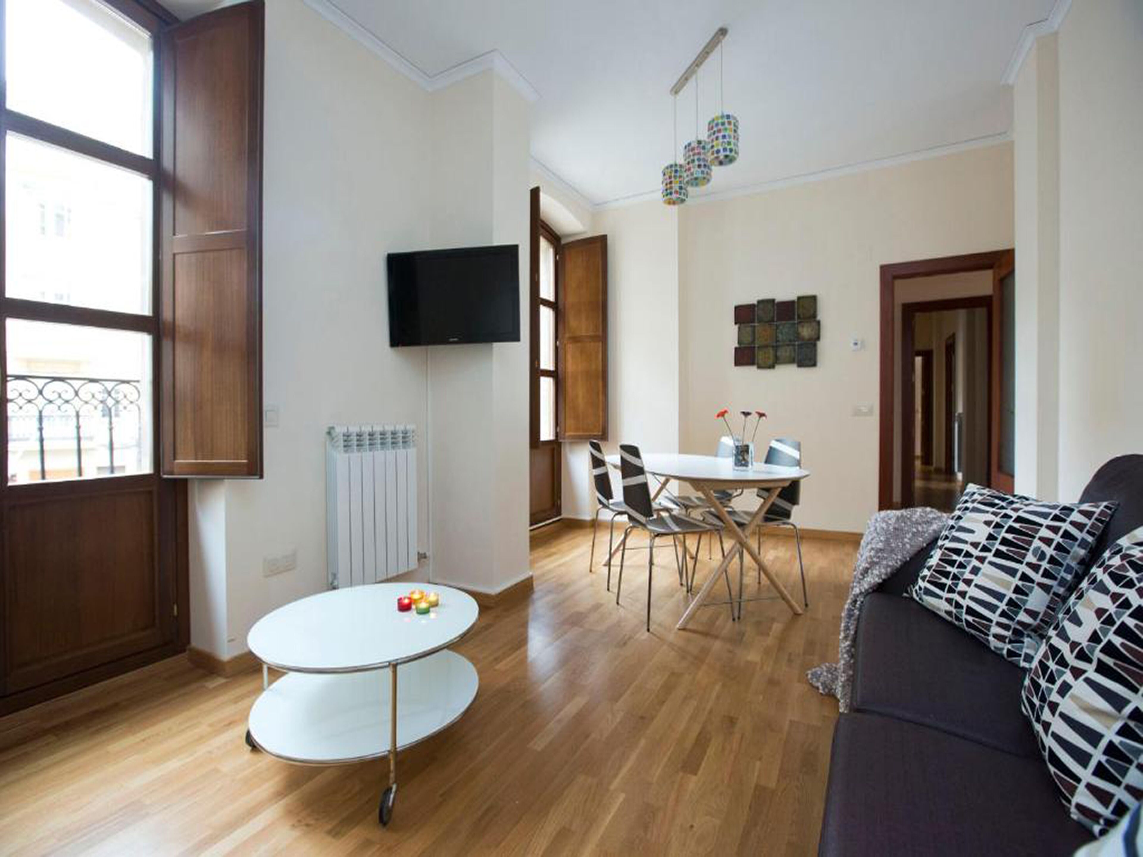 Una sala de estar con una mesa redonda, un sofá y un televisor montado en la pared.