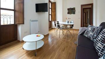 Una sala de estar con una mesa redonda, un sofá y un televisor montado en la pared.