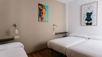 A hotel room with two single beds, a wall-mounted light, and two wall art pieces.