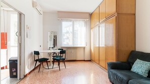 Un espace de vie compact comprenant un coin repas, un canapé et une fenêtre avec des stores.