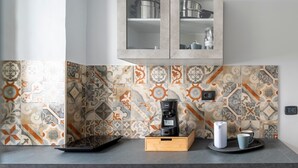 Una cocina con cafetera, una bandeja con taza y botella, y un armario con vajilla.