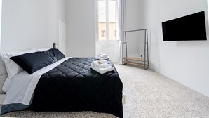 Una habitación de hotel con cama, televisión, ventana con cortinas y un espejo de pie.
