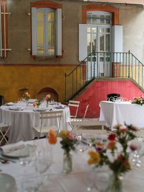 A dining area with round tables set for a meal, a staircase with a red wall, and a balcony with a railing. - Maison Bonnefoy Toulouse (Toulouse)
