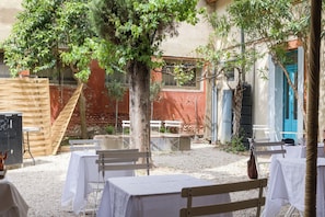 An outdoor seating area with tables and benches, surrounded by trees and a building with a blue door. - Maison Bonnefoy Toulouse (Toulouse)