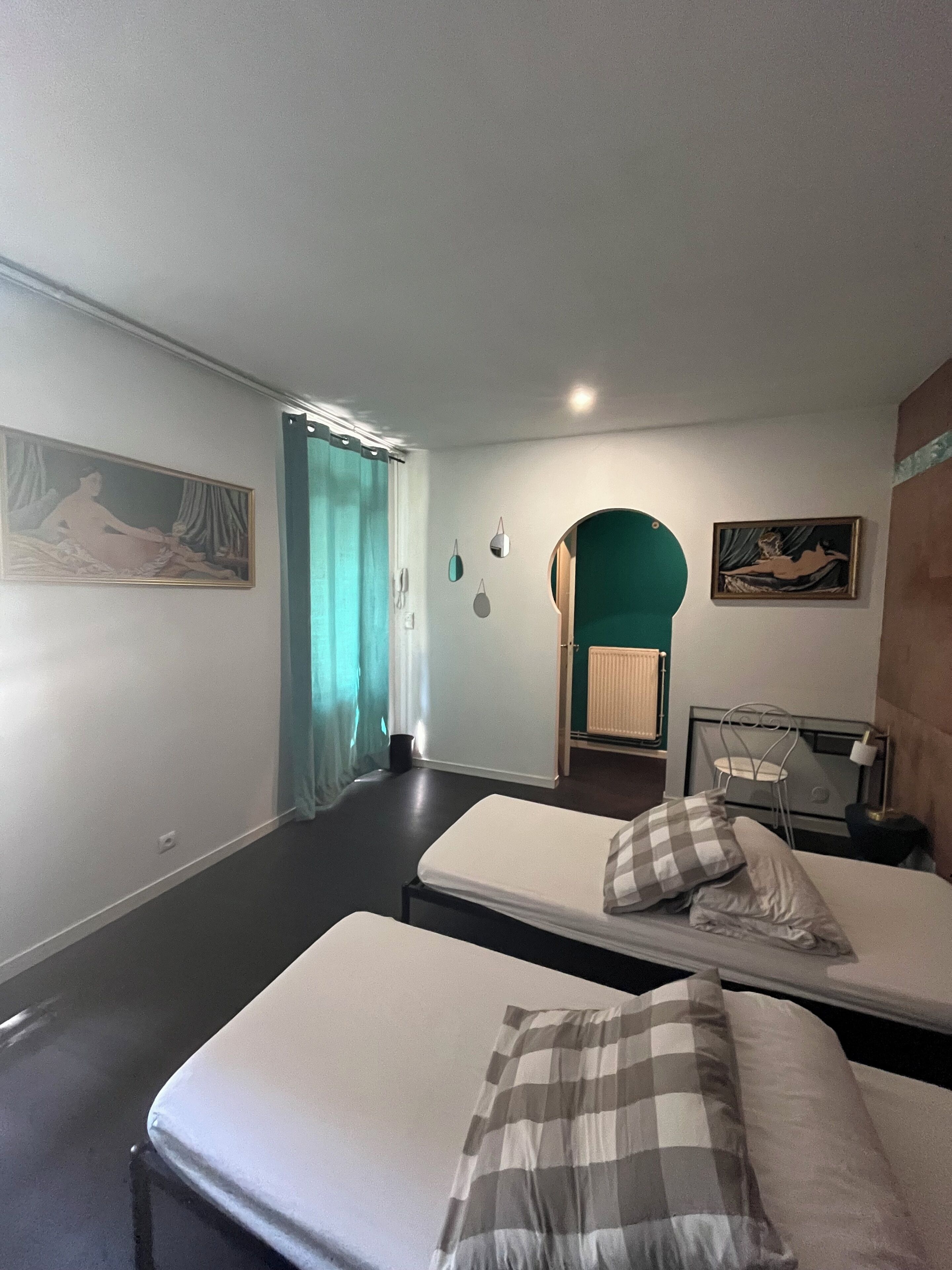 A room with two beds, a small table, a chair, and a painting on the wall.