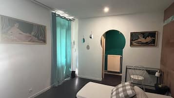 A room with two beds, a small table, a chair, and a painting on the wall.
