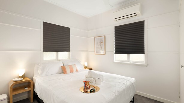 Une chambre d’hôtel bien aménagée, avec un lit, des tables de chevet, un climatiseur et une fenêtre équipée de stores.