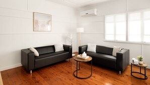 Un salon moderne avec deux canapés en cuir noir, une table basse en bois et un lampadaire blanc.