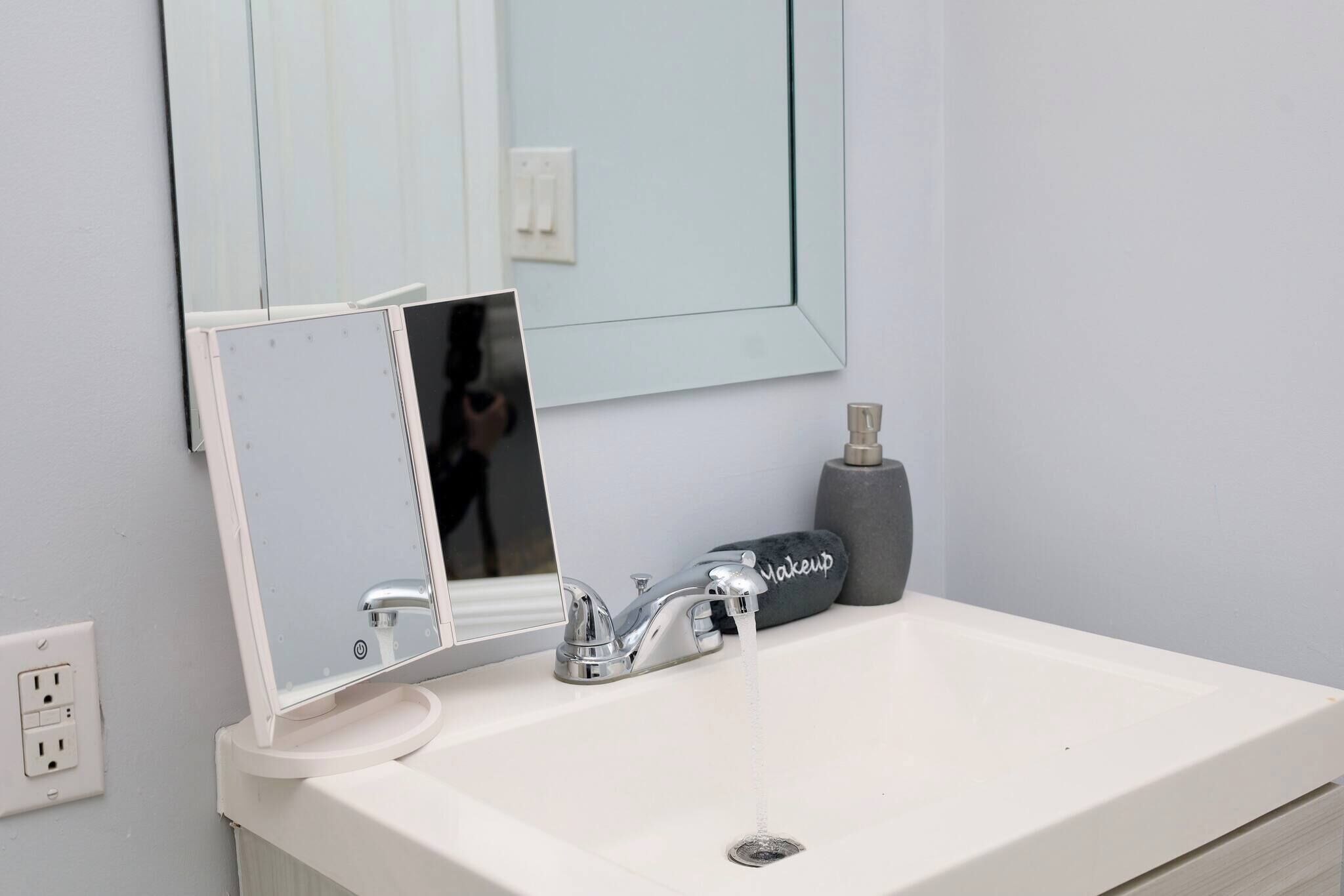 Une salle de bain avec un lavabo blanc, un miroir, un présentoir à maquillage et une serviette.