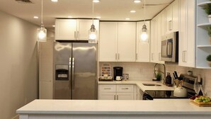 Una cocina moderna con gabinetes blancos, electrodomésticos de acero inoxidable, iluminación colgante y una zona de café.