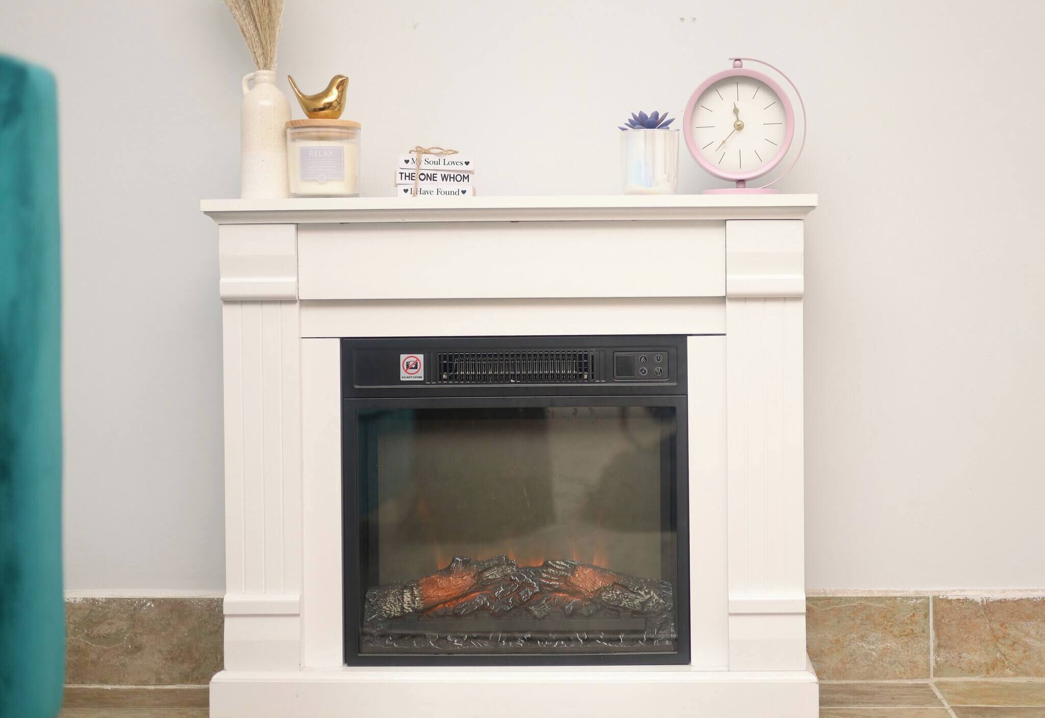 A white fireplace with a glass door, a clock, and decorative items on the mantel.