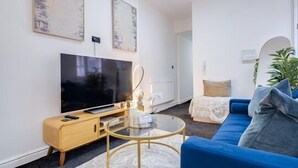 A modern living room with a flat-screen TV, a blue sofa, a glass coffee table, and artwork on the walls.