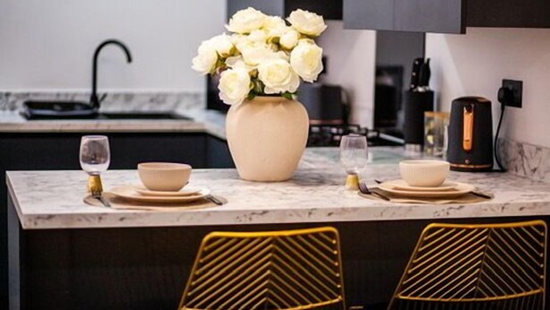 A modern kitchen with a marble countertop, a vase of white flowers, and two chairs with a geometric design.