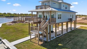 A two-story waterfront house with a balcony, a deck, and a view of the water. - Modern Matagorda Getaway – 4 King Bedrooms, Canal Access & Minutes to the Beach (Matagorda)