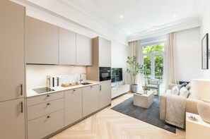 Une cuisine moderne dotée d’appareils électroménagers intégrés, un coin repas avec un canapé et une table basse, et une vue sur la verdure environnante.