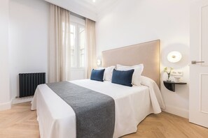 Habitación de hotel con una cama grande, una mesita de noche con lámpara, un radiador y una ventana con cortinas.