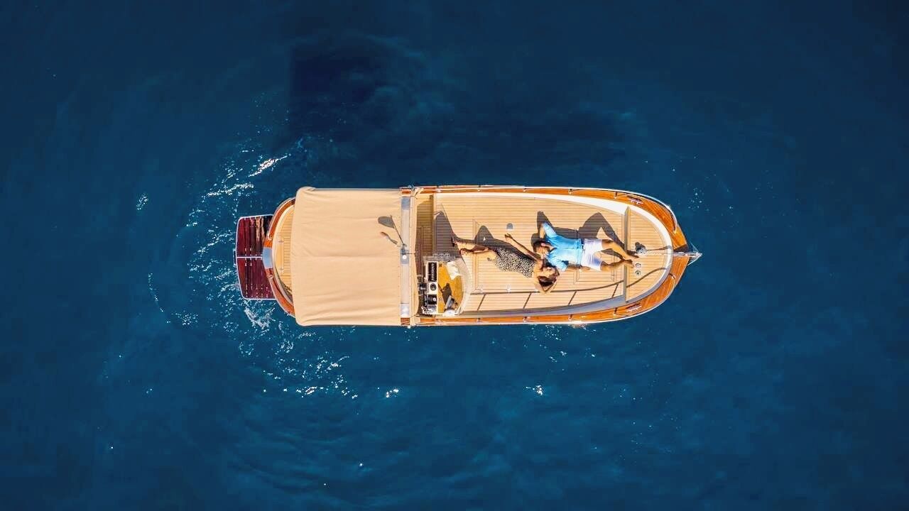 A small boat with two people lying on the deck, surrounded by water.